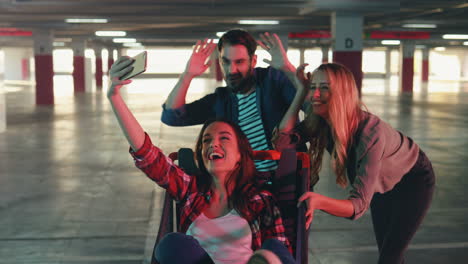 grupo joven de alegres amigos caucásicos divirtiéndose en un estacionamiento vacío con un carrito de supermercado y tomando selfies