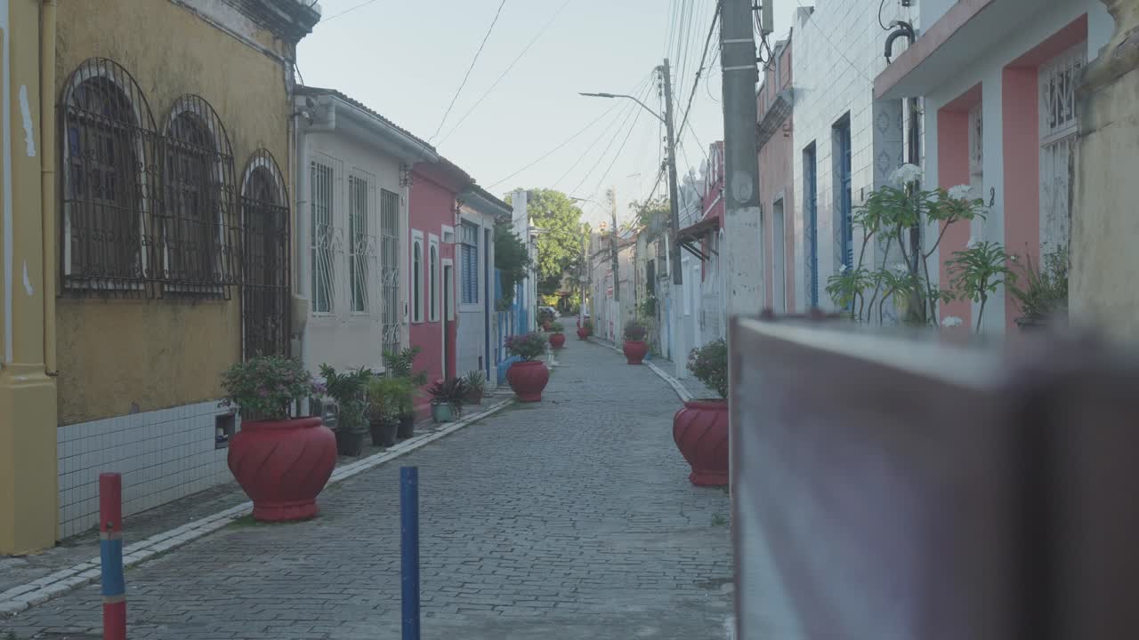 Village street with colorful houses, potted plants, late afternoon, tree illuminated by the sun in the background