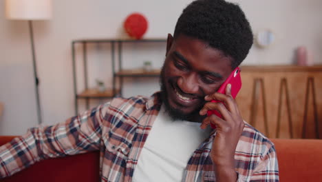 Young-adult-african-american-man-enjoying-talking-mobile-phone-conversation-with-friends-at-home