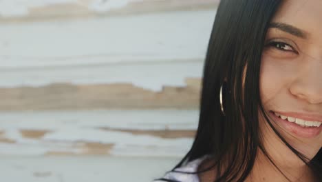 Portrait-of-smiling-hispanic-woman-in-front-of-weathered-wooden-wall-in-sun,-copy-space,-slow-motion