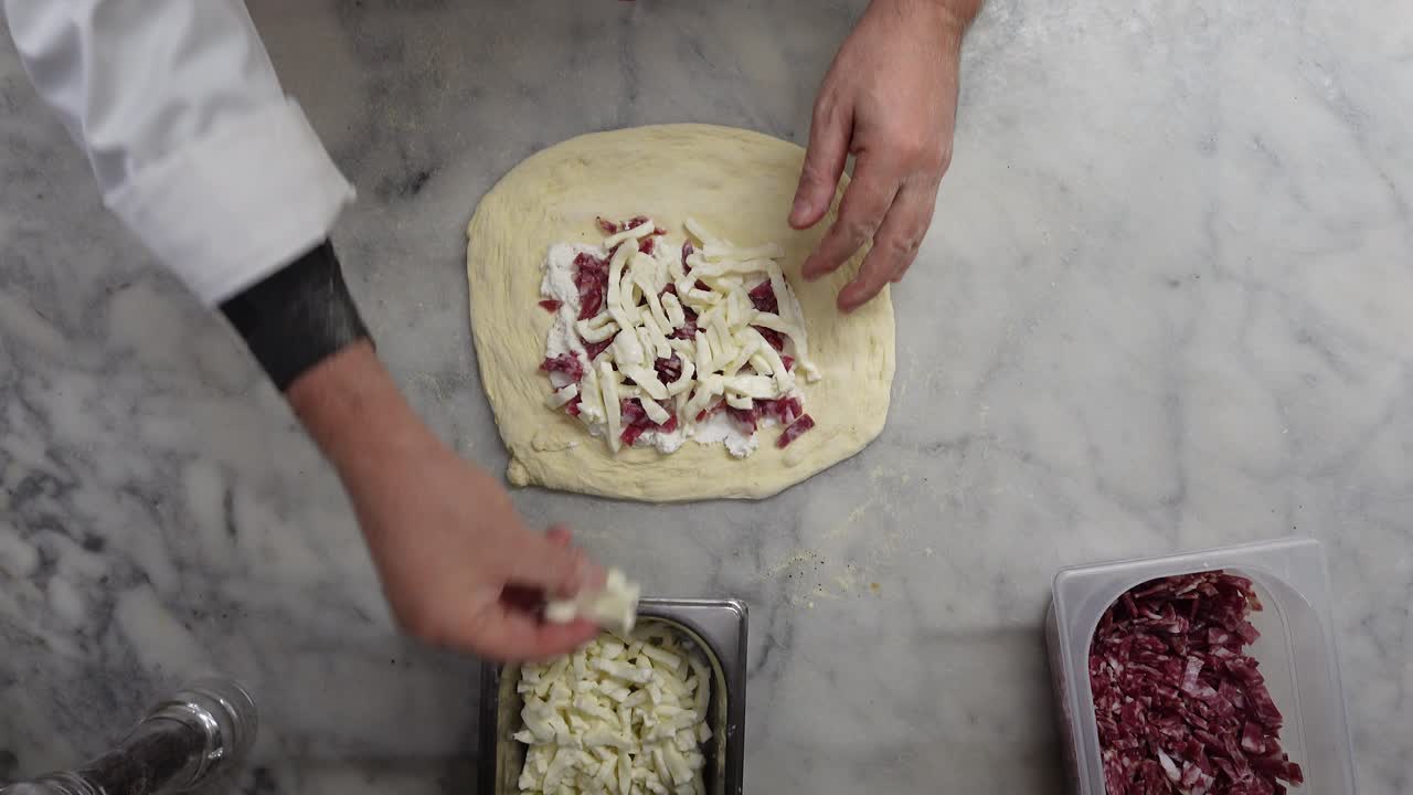 Chef italiano che prepara un calzone o una pizza ripiena con ricotta, mozzarella e salame. Inquadratura dall'alto.