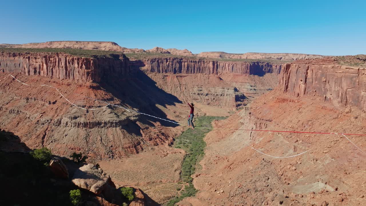 Funambolo cammina su slackline sopra il canyon di Moab con uno scenario limpido sotto un cielo azzurro