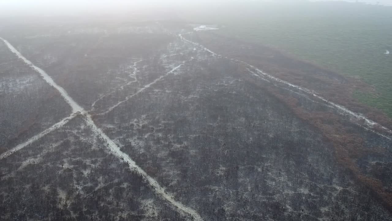 A slight pan aerial shot of a blackened Australian landscape, on the edge of the fire grounds