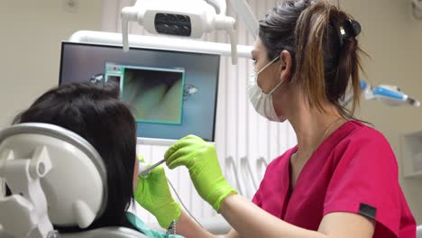 Young-female-dentist-examining-the-mouth-of-a-patient-with-an-intraoral-camera-and-showing-image-on-the-screen.-Shot-in-4k