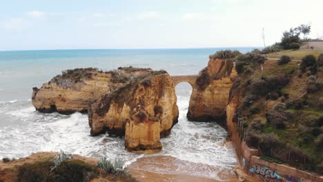 puente de piedra primitivo arqueado en la playa de estudiantes en lagos, algarve, portugal - antena aérea de ángulo bajo