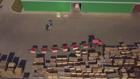 red tractor with trailers full of red apples at farmland going near empty wooden crates. farmhouse, tractor with trailers and a lot of crates outdoors. aerial view