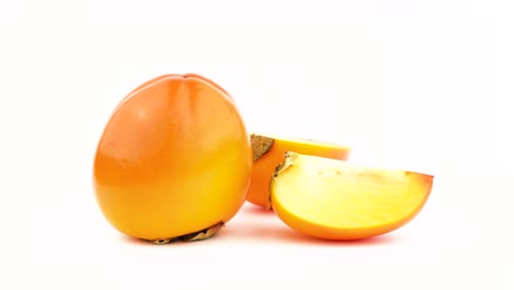 one whole persimmon fruit with two kaki halves. rotating on the turntable. isolated on the white background. close-up. macro.