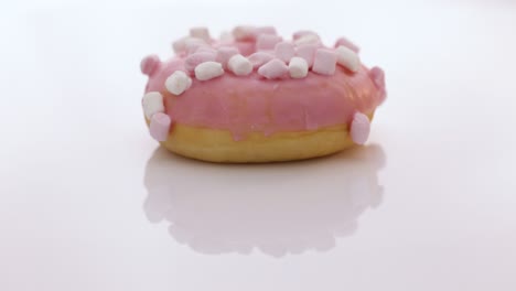 rotating close-up shot of pink tasty delicious sweet donut with colorful sprinkles on white background. tasty rotating donut on white background. dessert. colorful frosted pink doughnut