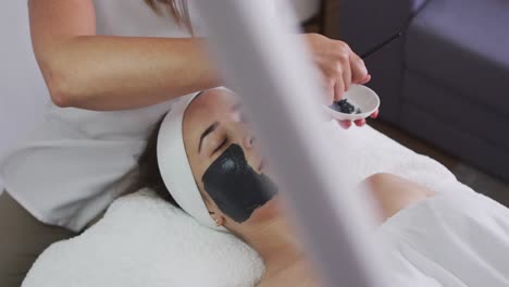 caucasian woman lying back while beautician gives her a face mask