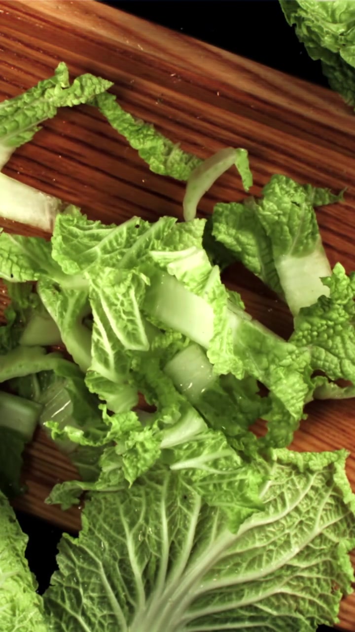 Chopping Fresh Napa Cabbage Leaves on a Wooden Cutting Board