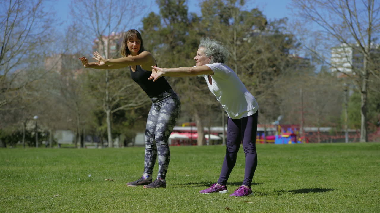 una mujer mayor sonriente entrenando con una entrenadora en el parque de verano.