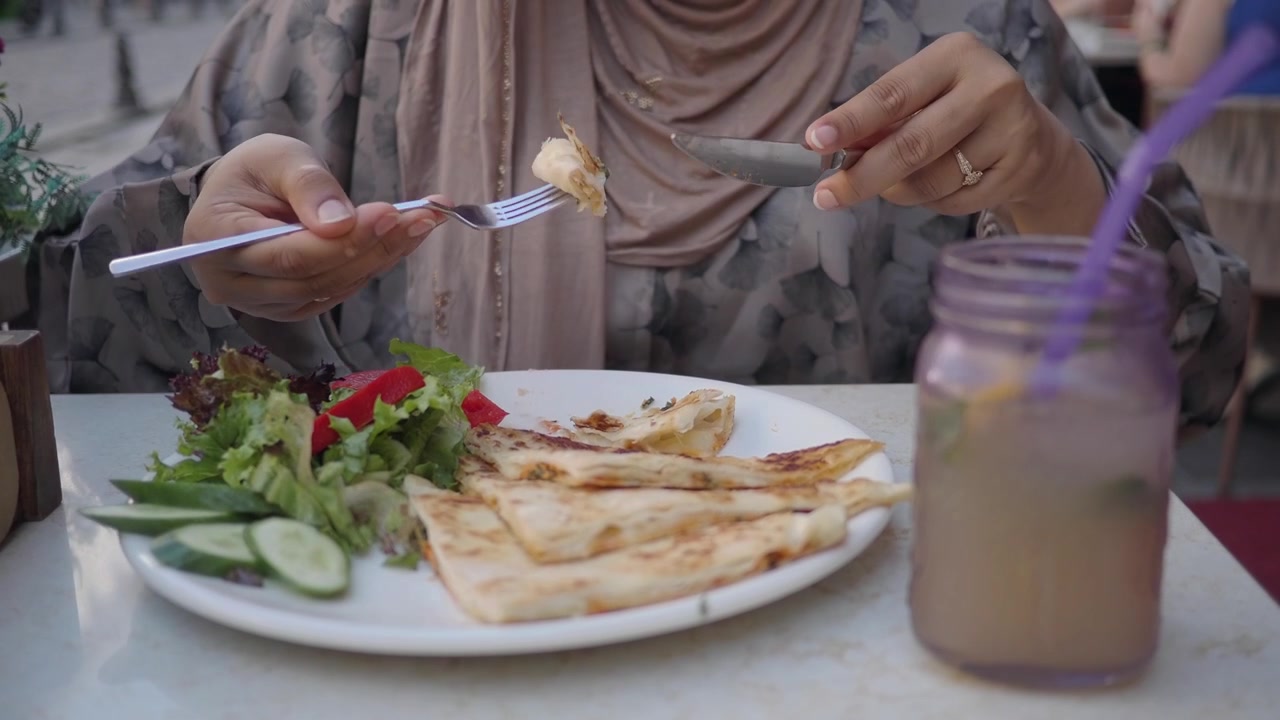 Woman in Hijab Eating Flatbread and Salad at Outdoor Restaurant