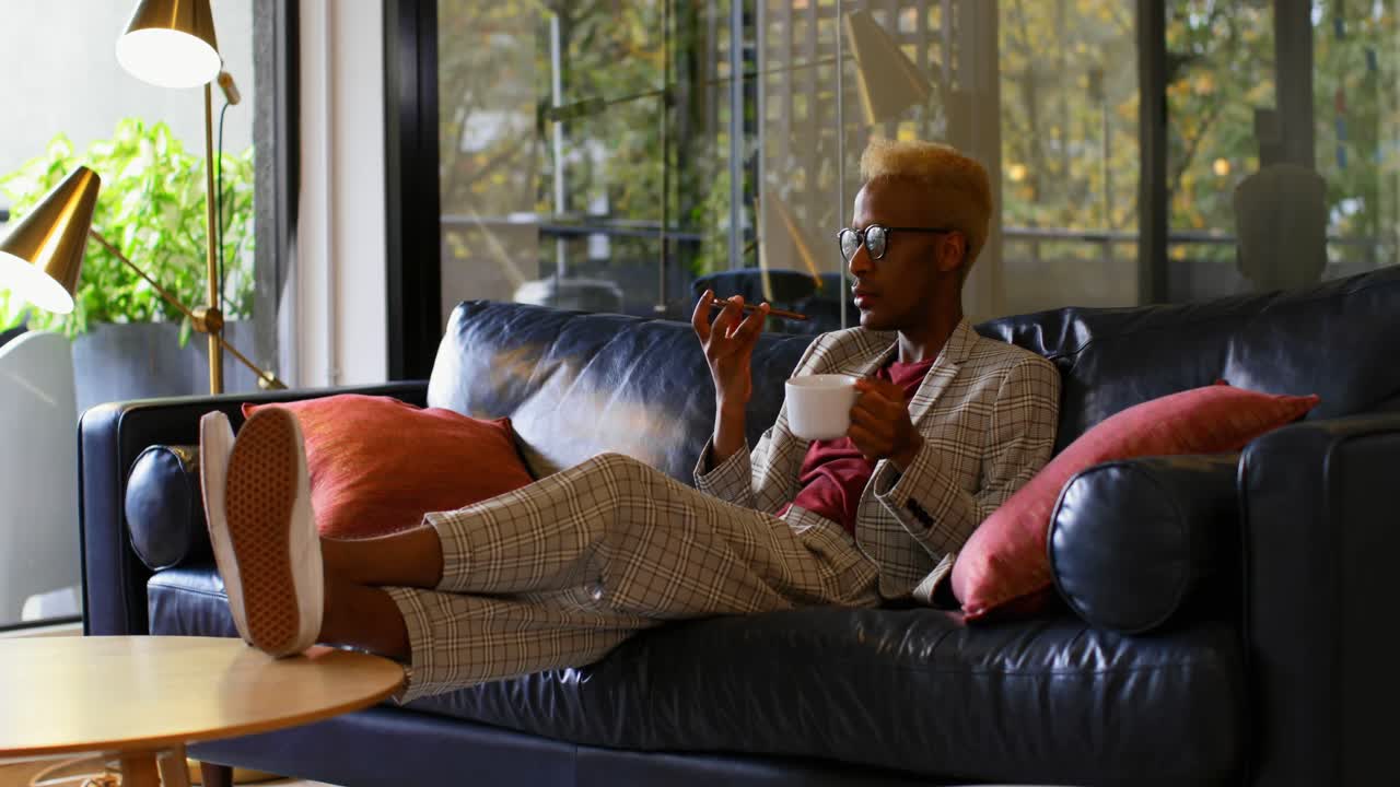 Giovane uomo d'affari nero che beve caffè e parla al telefono cellulare in un ufficio moderno 4k