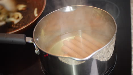 Hot-dogs-are-cooking-in-a-saucepan-as-onions-are-fried-and-stirred