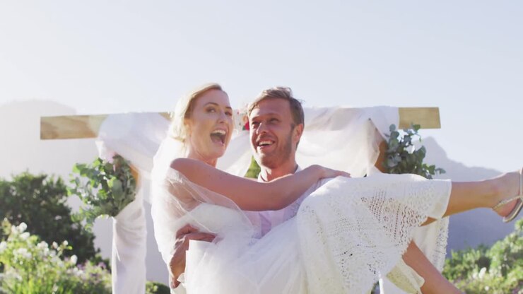 Happy caucasian husband carries newly wed bride and walks down altar outdoors