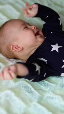 nice healthy boy lies on the bed. infant baby being active, rubs little face and smiles sweetly. white backdrop. vertical video