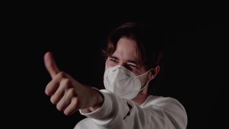 trendy young man unsure thumb gesture wearing mask, close, black background