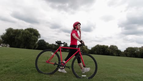 caucasian female cyclist in red top walking with her bike in a park in slow motion