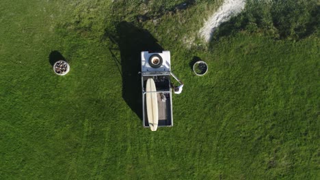vista superior de un hombre que sale de su landrover que está estacionado en hierba verde y saca su tabla de surf que termina con un paisaje con vista al océano