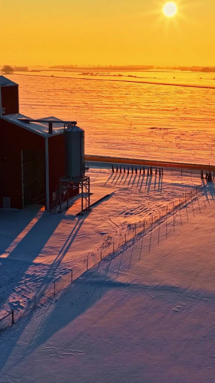 Kornsiloer på et snødekt jorde under soloppgang som kaster lange skygger i landlige omgivelser