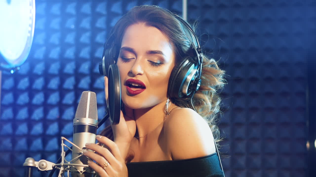 Vinnitsa, Ukraine - May 2019: Audio recording studio. Woman with headphones and studio microphone singing. Slow motion