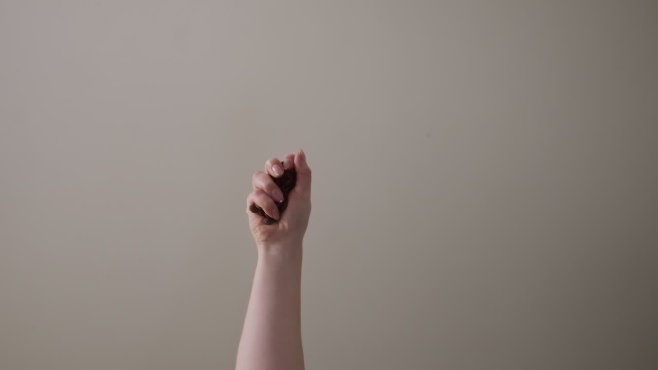 Primo piano di una mano che lascia cadere pezzi di cioccolato in interni su sfondo neutro.