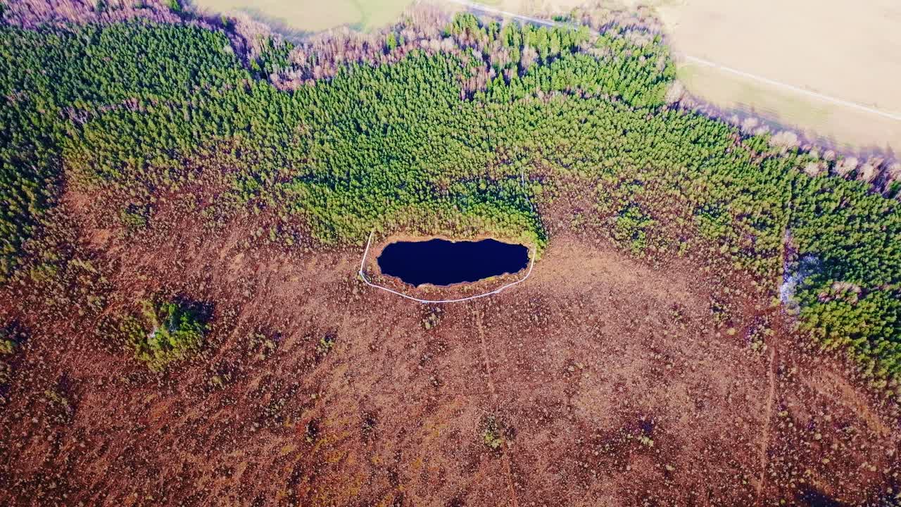 Symmetrical drone shot small lake embedded in Kalnansu bog in early spring light