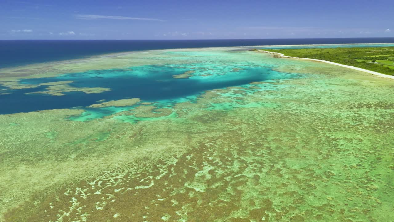 石垣島の鮮やかなサンゴ礁、透き通ったターコイズブルーの海、そして明るい青空の下の熱帯の海岸線の息をのむようなドローン映像。