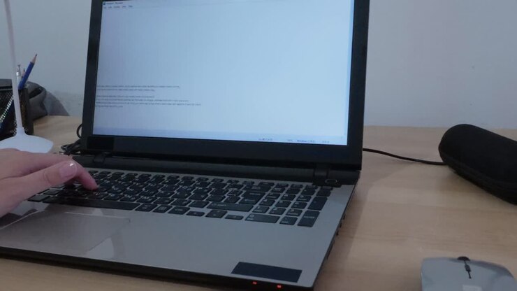 Nahaufnahme von Händen, die auf einer Laptop-Tastatur tippen, mit hebräischem Text auf dem Bildschirm.