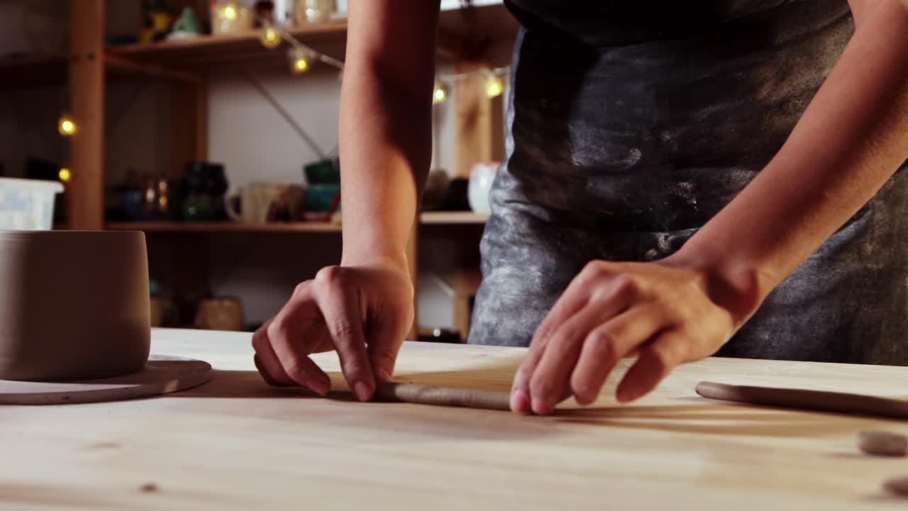 Pottery in the studio - young woman cuts off a piece of clay for making a handle for cup