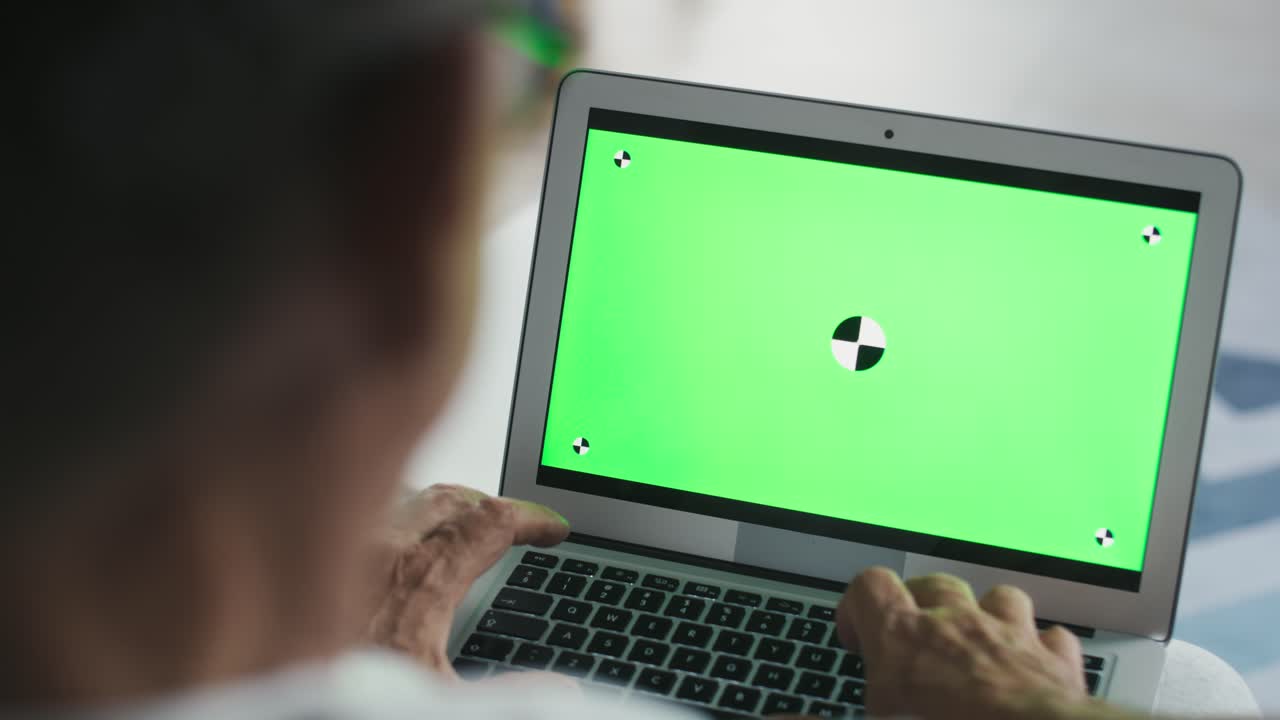 un hombre caucásico mayor sentado en el sofá y usando una computadora portátil.