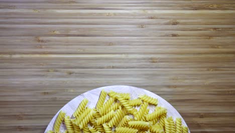 02:05 - pasta de fusilli sin cocer girando sobre una tabla de cortar en blanco, en bucle