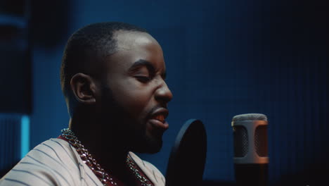 close up of the young handsome singer singing gently his vocal part in the microphone while recording a song in the dark sound studio