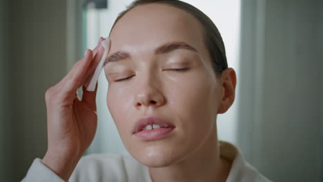portrait woman cleansing skin at home. girl applying lotion on face