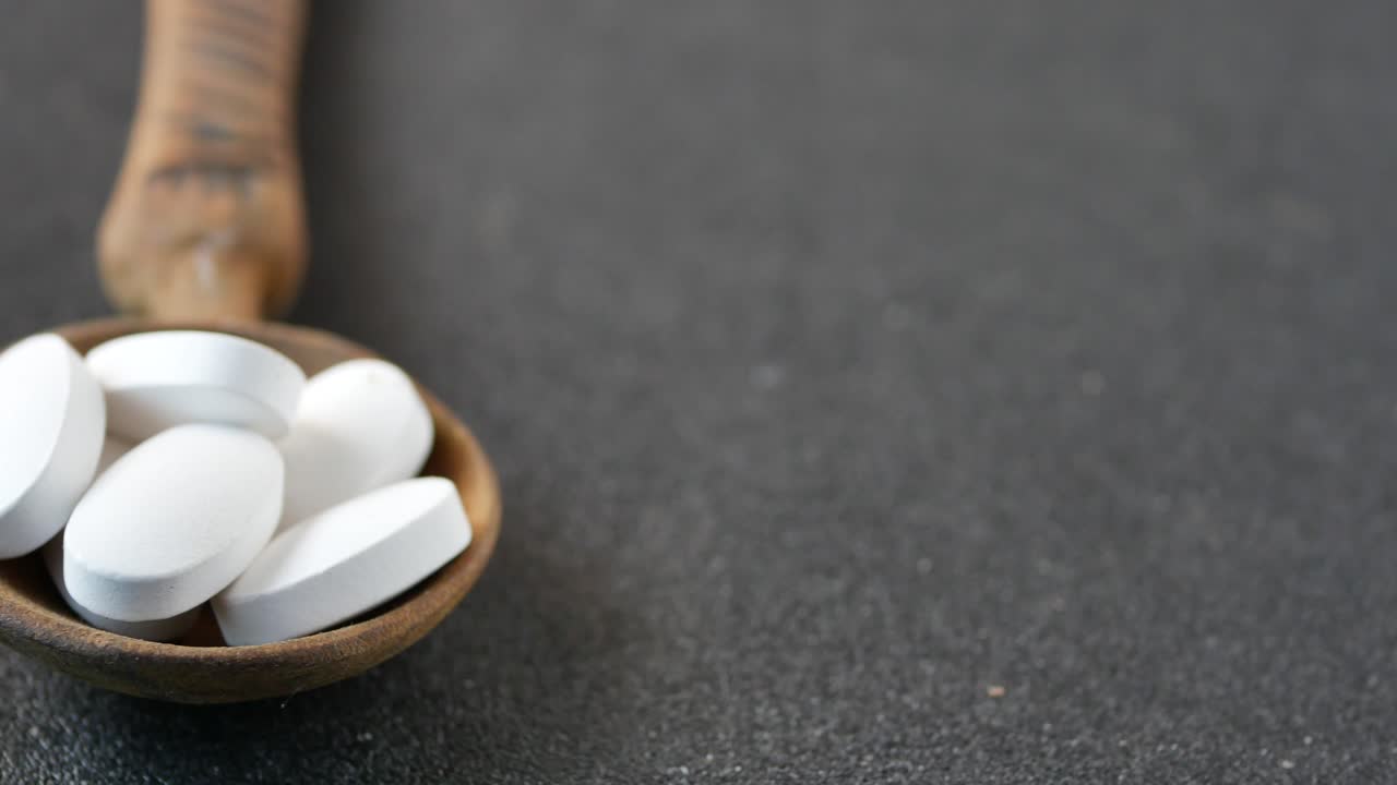 pastillas blancas y cápsulas marrones en cucharas de madera