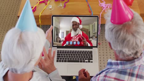 pareja de adultos mayores caucásicos con sombreros de fiesta en la computadora portátil video chat durante la navidad en casa