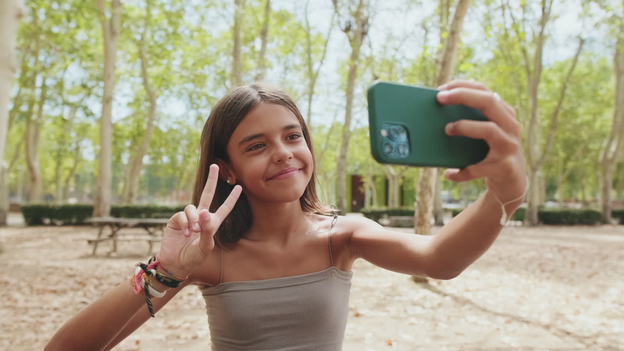 Happy Young Girl Takes a Selfie and Makes a Peace Sign in a Park