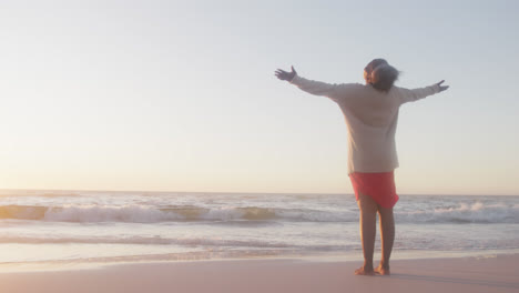gelukkige senior afro-amerikaanse vrouw breidt haar armen uit op het strand, in slow motion, met kopieerruimte.