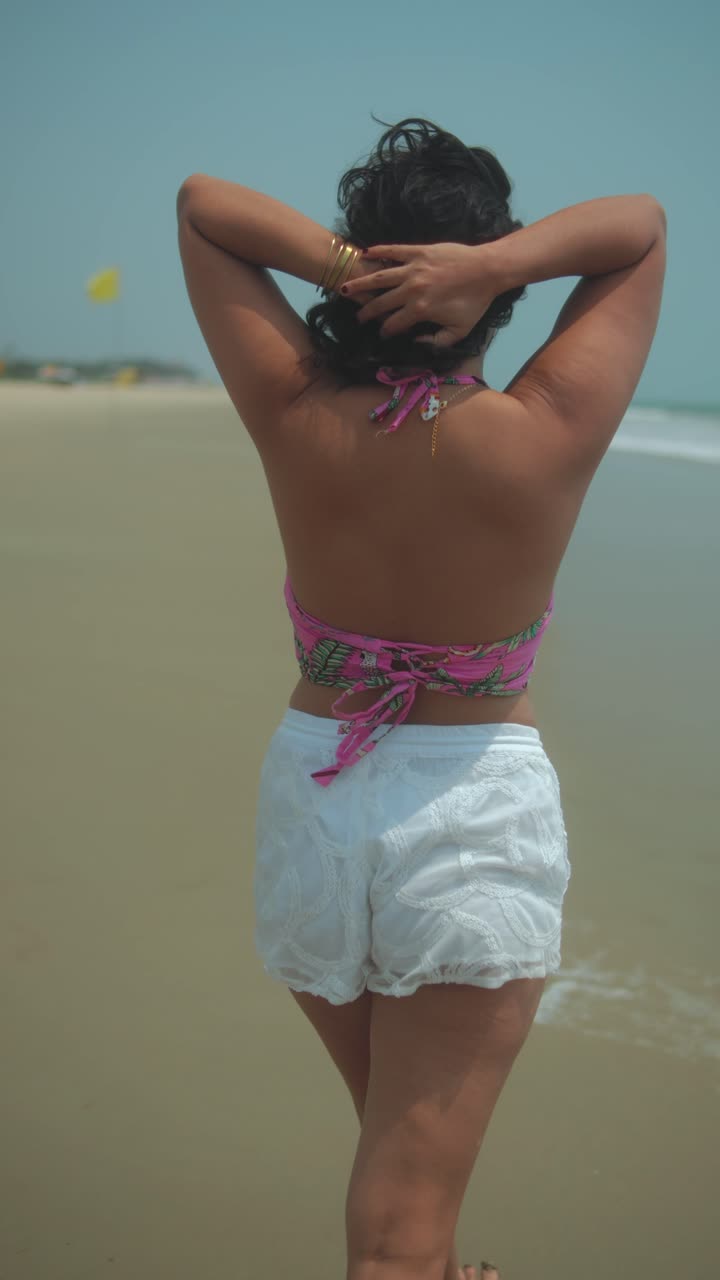Young woman walking along the beach, relaxing in the sun, with a breeze flowing through her hair