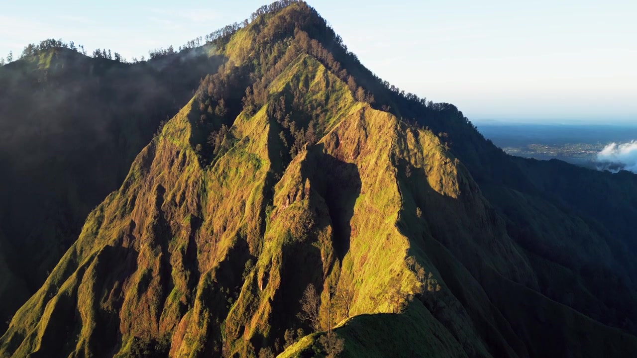Luce dorata del mattino con nuvole soffici che passano su una stretta cresta con ripidi pendii erbosi attraverso un terreno montuoso accidentato, filmato aereo con drone in avvicinamento.