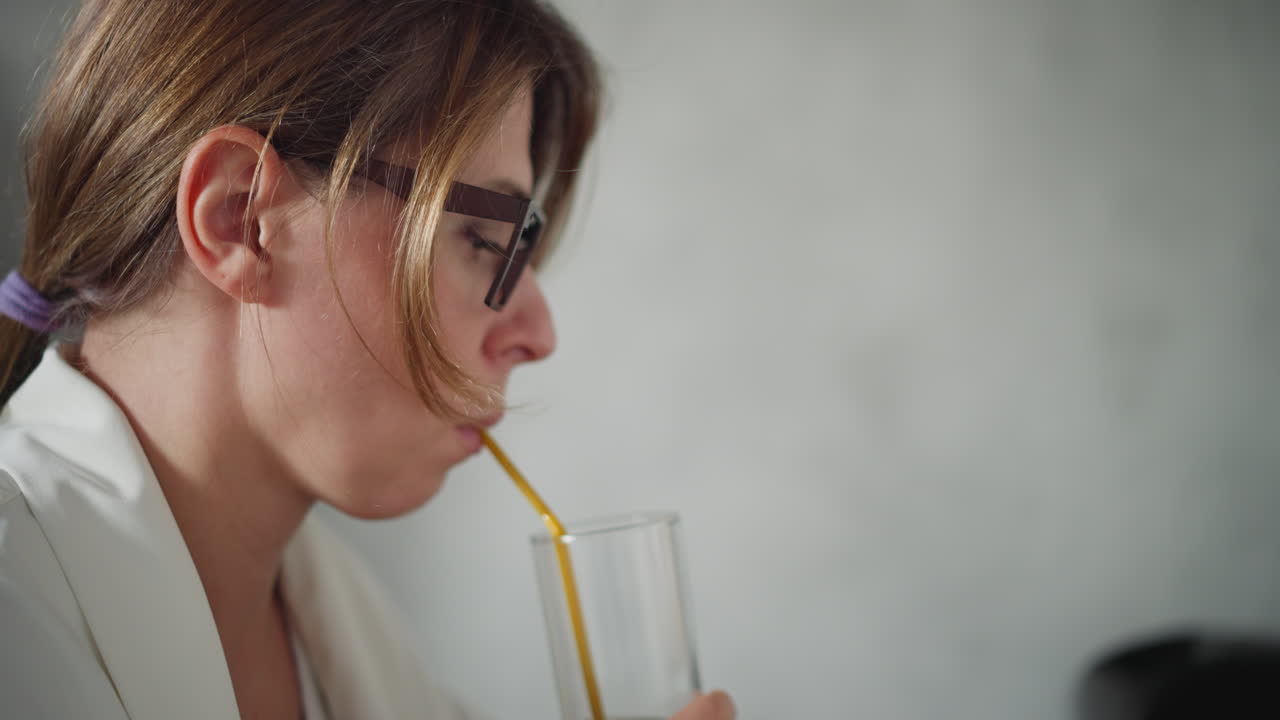 Close up of lady in white top sipping dark juice with yellow straw focused on drink blur background featuring soft light and indistinct black item
