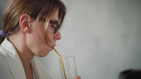 close up of lady in white top sipping dark juice with yellow straw focused on drink blur background featuring soft light and indistinct black item