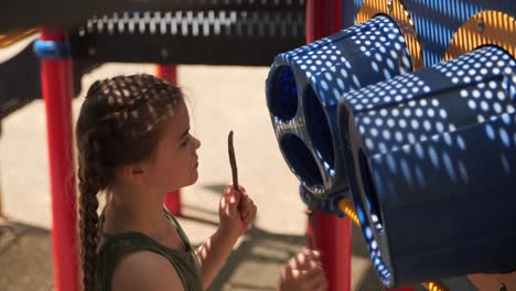 young girl playing plastic drums in a children’s playground with sticks