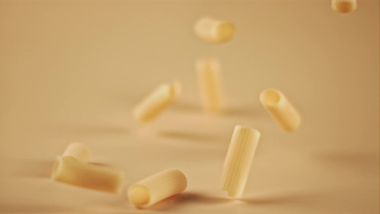 Pasta secca che cade al rallentatore su sfondo beige