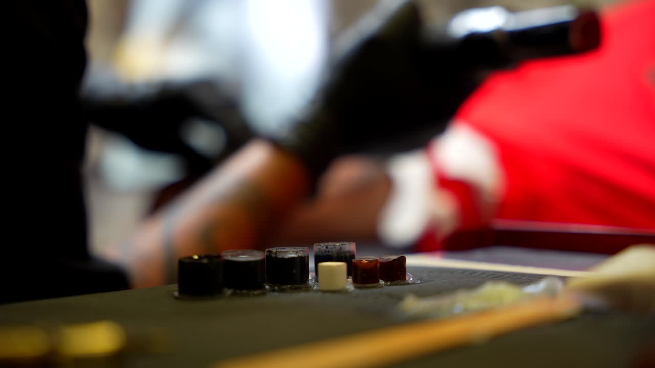 Handheld shot of a tattoo artist using different colours of ink at work in a studio
