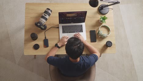 top view of a male color grading sitting in the workspace using a laptop next to the camera editing the video at home