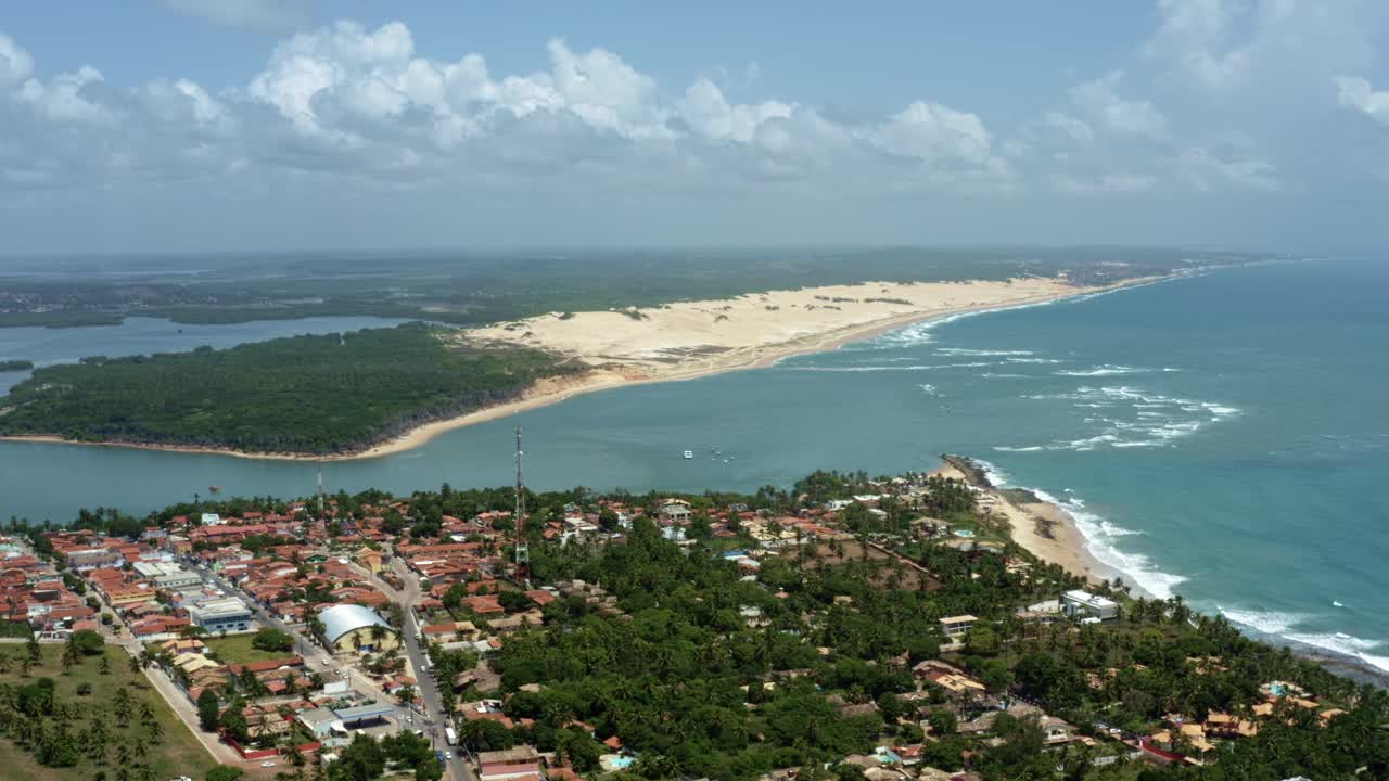 Right trucking aerial drone wide shot of the tropical beach town of Tibau do Sul in Rio Grande do Norte, Brazil with the Malemb&aacute; Sand Dunes, Atlantic Ocean, and Guara&iacute;ras Lagoon in the background