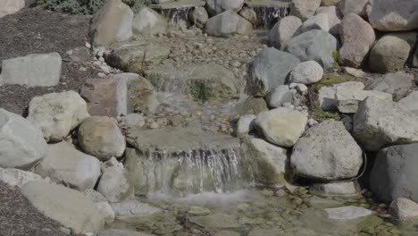 small handmade garden waterfall made with rocks and pebbles, clear water stream shimmering in sunlight