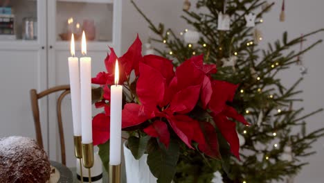 Rote-Weihnachtssternblume-In-Einem-Weißen-Topf-Im-Wohnzimmer,-Umgeben-Von-Kerzen-In-Einem-Kerzenständer-Und-Einer-Geschmückten-Weihnachtskiefer