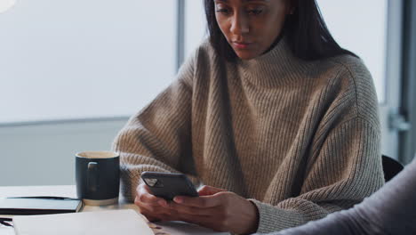 mujer de negocios que usa un teléfono móvil como colega masculino trabaja en una computadora portátil en primer plano